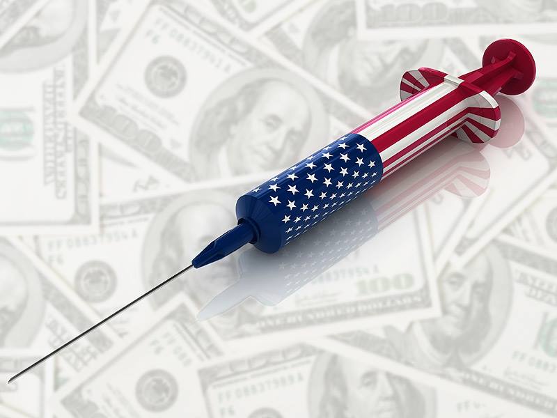 A syringe decorated with an American flag lying on top of many $100 notes.